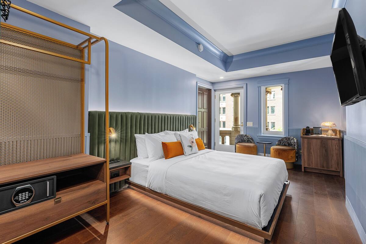Quarto de hotel com uma cama, uma escrivaninha, uma televisão e uma janela.