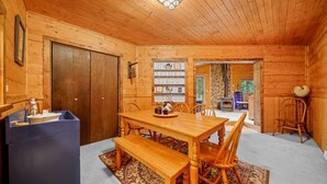 A wooden cabin interior with a dining table, chairs, a bench, a bookshelf, and a stone fireplace. - A-Frame at Arrowhead (Cimarron)