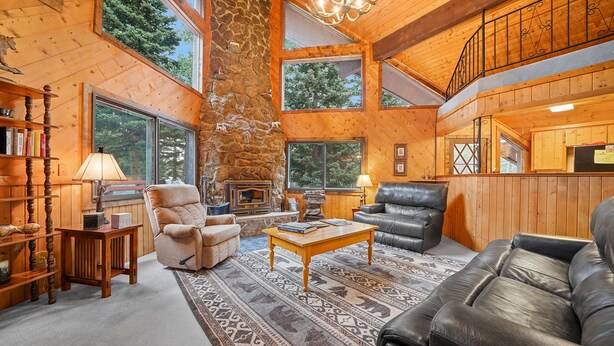 A cozy cabin interior with a fireplace, leather sofas, a wooden coffee table, and a stone wall. - A-Frame at Arrowhead (Cimarron)