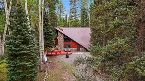 A cabin with a red roof and stone walls, surrounded by tall trees. - A-Frame at Arrowhead (Cimarron)