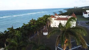 A coastal property with a large white building, palm trees, and the ocean in the background.