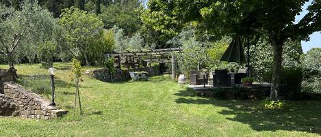 Un jardín con muro de piedra, mobiliario exterior y un pérgola.