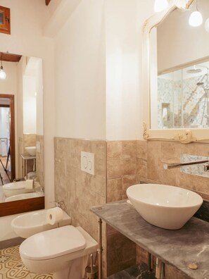 Une salle de bain équipée de toilettes, d’un bidet et d’un grand lavabo avec un miroir au-dessus.