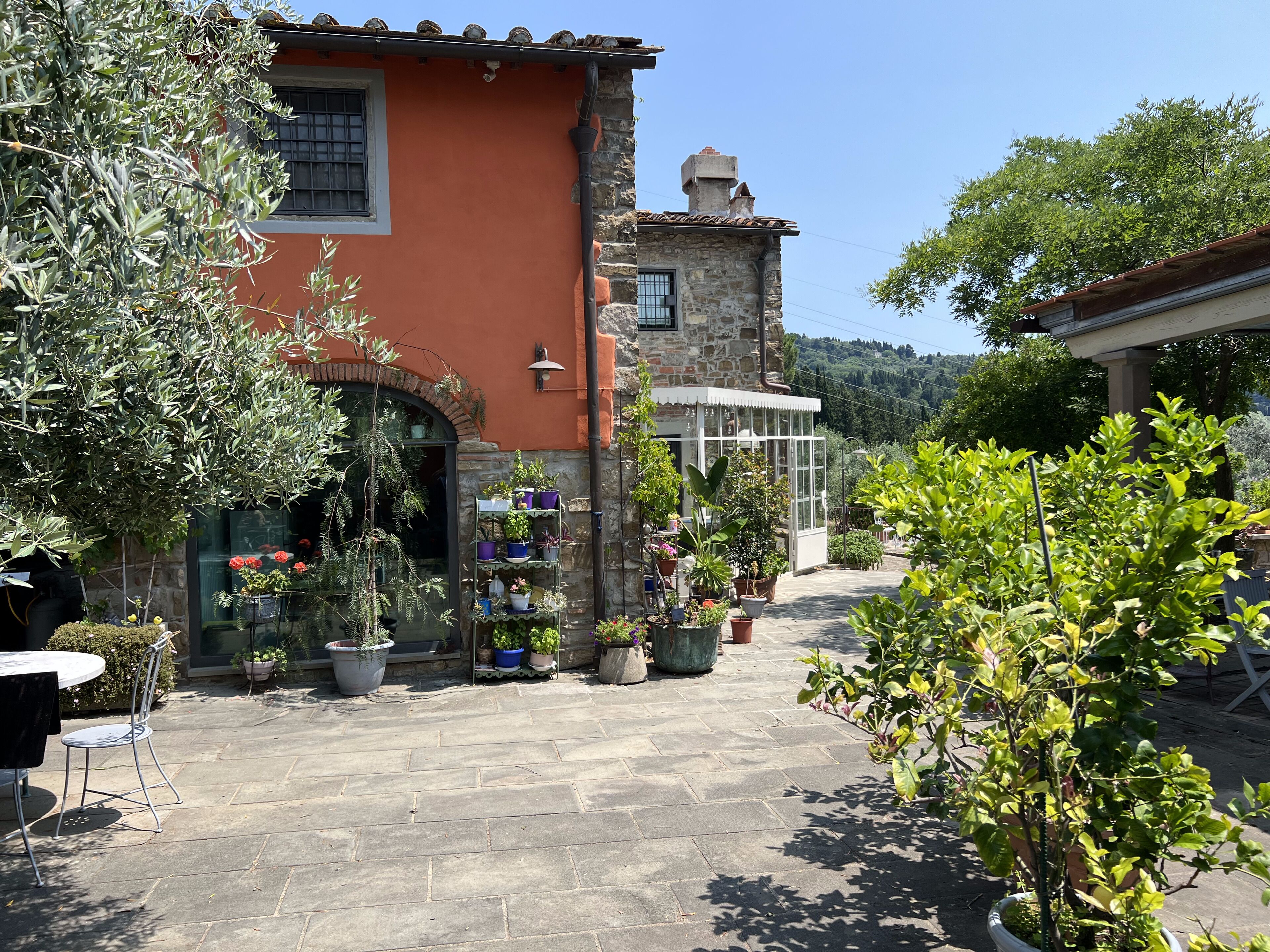 Une cour avec un bâtiment en pierre, des plantes en pot et une table avec des chaises.