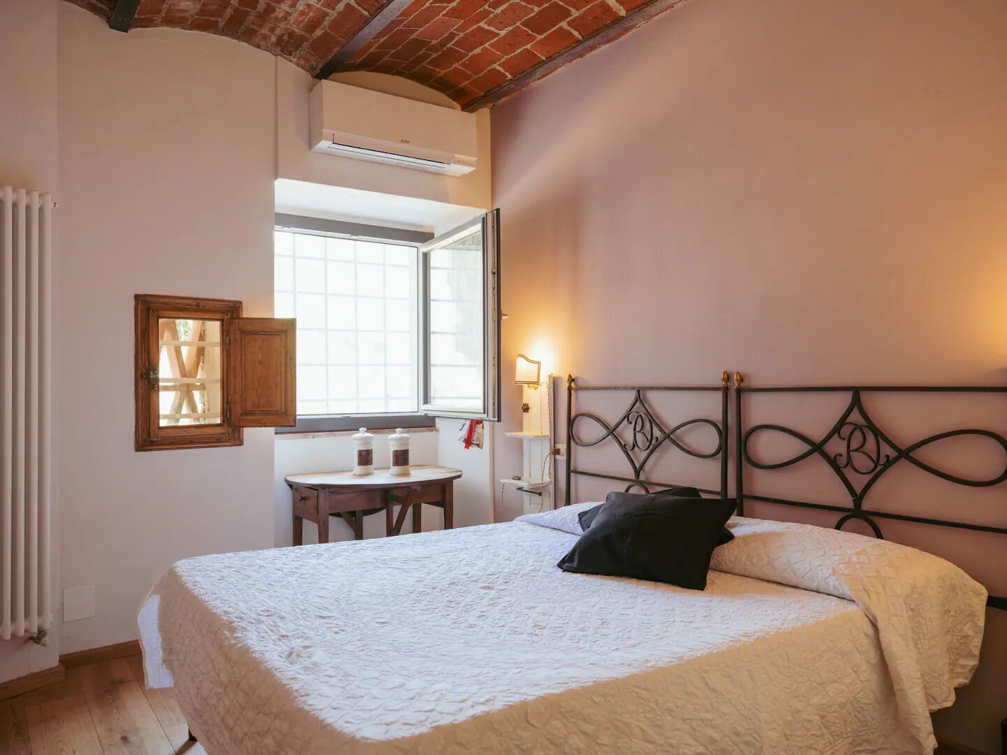 A bedroom with a bed, a small table, a window, and a radiator.