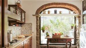 A kitchen with a stone backsplash, wooden cabinets, and a window with a view of greenery. - Villa Peramonda (Toscana)
