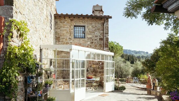 A stone building with a glass conservatory, potted plants, and outdoor seating. - Villa Peramonda (Toscana)