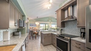 A modern kitchen with granite countertops, stainless steel appliances, and a dining area with a view. - Private Waterfront Oasis w/Heated Pool/Hot Tub & Dock, Close to Everything! (Naples)