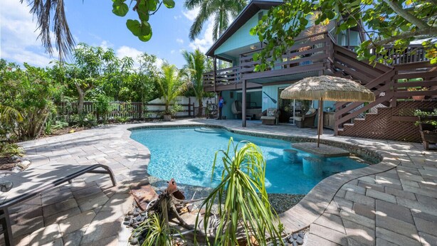 A swimming pool with a wooden deck, surrounded by lush greenery and a multi-level wooden structure. - Private Waterfront Oasis w/Heated Pool/Hot Tub & Dock, Close to Everything! (Naples)