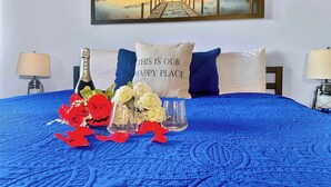 A neatly made bed with a blue bedspread, a bottle of champagne, and decorative flowers.