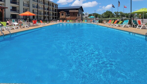 A swimming pool with lounge chairs and umbrellas, surrounded by buildings with balconies and flags. - 404 - Walk to Landing, Convention Center & Cox Med (Branson)
