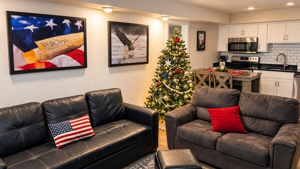 A living room with two leather sofas, a Christmas tree, and a kitchen in the background.