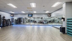 Ein Fitnessraum mit Spiegelwand, Trainingsgeräten und einem Fernseher.