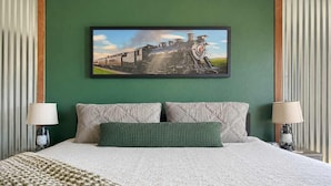 A hotel room with a bed, two bedside lamps, a green wall, and a framed picture of a train. - 408 - Cozy, Pet friendly walk to Landing, King bed (Branson)