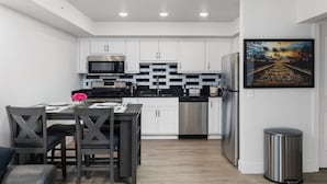 A modern kitchen with white cabinets, black countertops, stainless steel appliances, and a dining area with dark chairs and a table. - 408 - Cozy, Pet friendly walk to Landing, King bed (Branson)