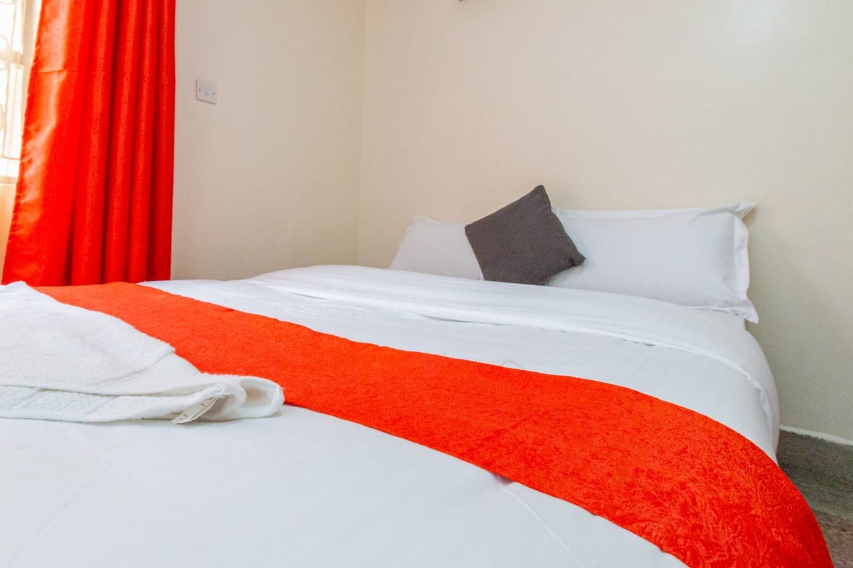 A neatly made bed with white and orange bedding, a grey pillow, and a white towel on the side.