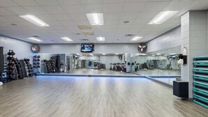 Une salle de sport avec un plancher en bois, des miroirs, du matériel d’exercice et un téléviseur fixé au plafond.