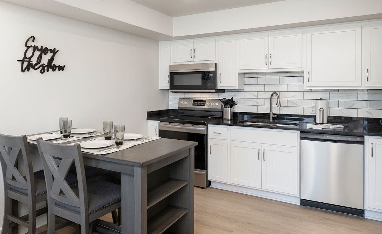 A modern kitchen with white cabinets, stainless steel appliances, and a dining table set for four.