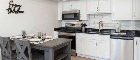 A modern kitchen with white cabinets, stainless steel appliances, and a dining table set for four.