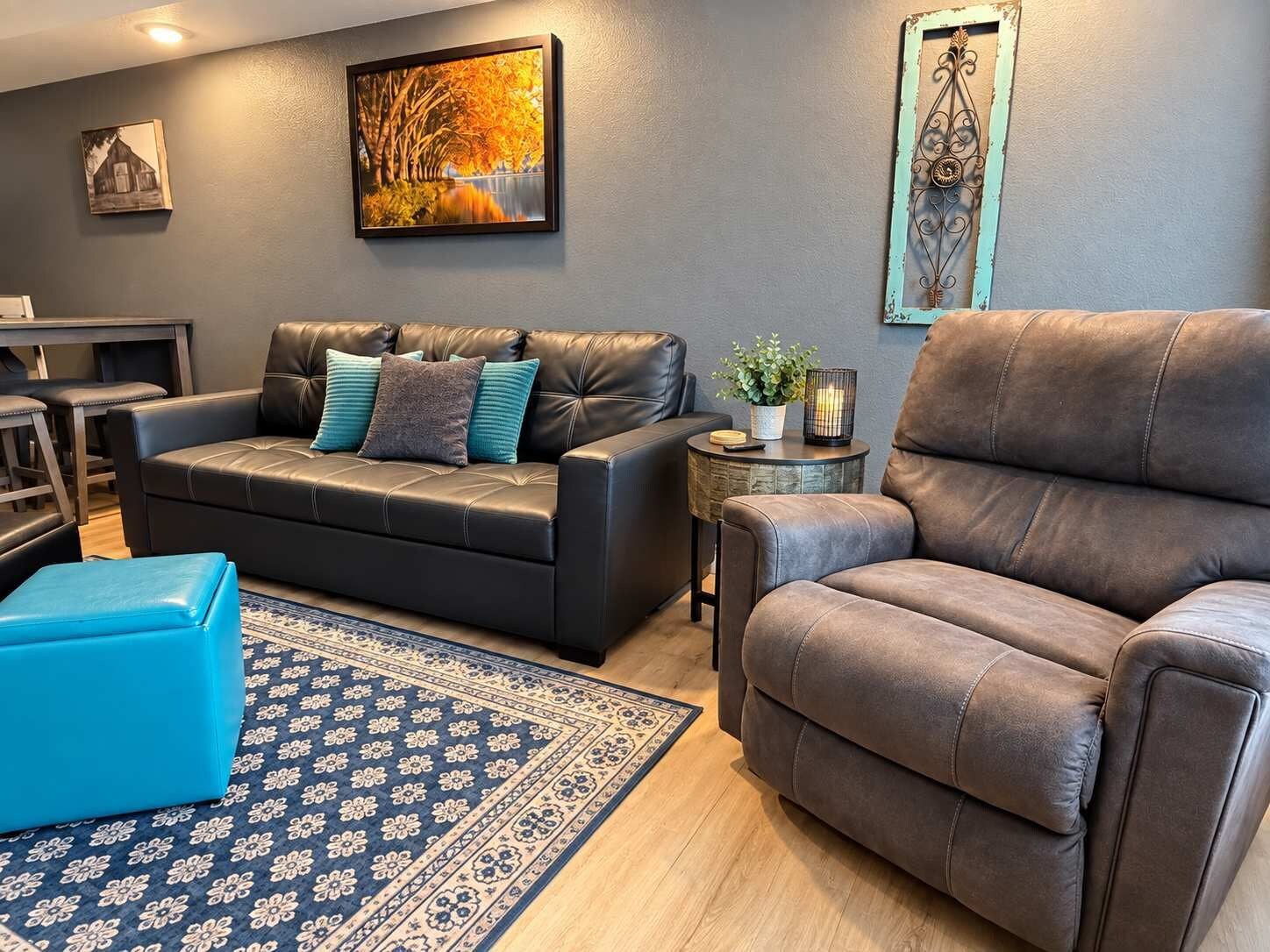 Un salon comprenant un canapé, un fauteuil, une petite table d’appoint avec une plante et un tapis.