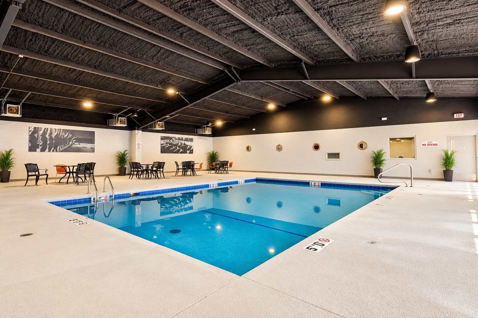 Ein Innenpool mit Fliesenboden, umgeben von Liegestühlen und Tischen, und einer Decke mit sichtbaren Balken.