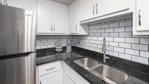 A modern kitchen with white cabinets, a stainless steel refrigerator, a double sink, and a black and white tiled backsplash. - 106-Walk to Downtown & Landing | Pools + No Stairs (Branson)