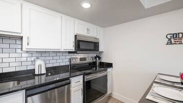 A compact kitchen with white cabinets, a black countertop, stainless steel appliances, and a dining area with a table set for two.