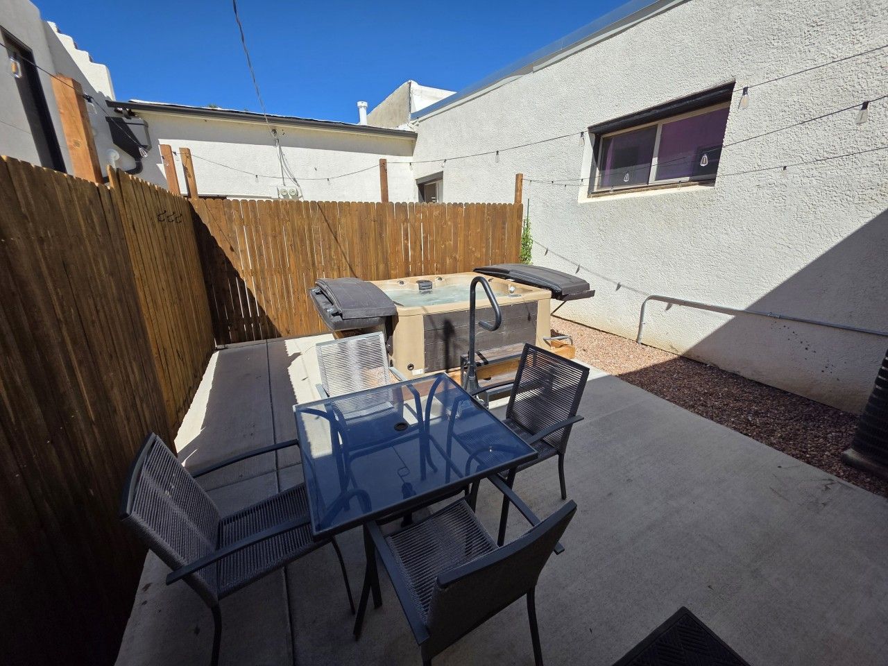 An outdoor patio with a barbecue grill, a glass table, and metal chairs.
