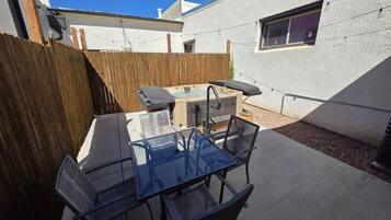 An outdoor patio with a barbecue grill, a glass table, and metal chairs.