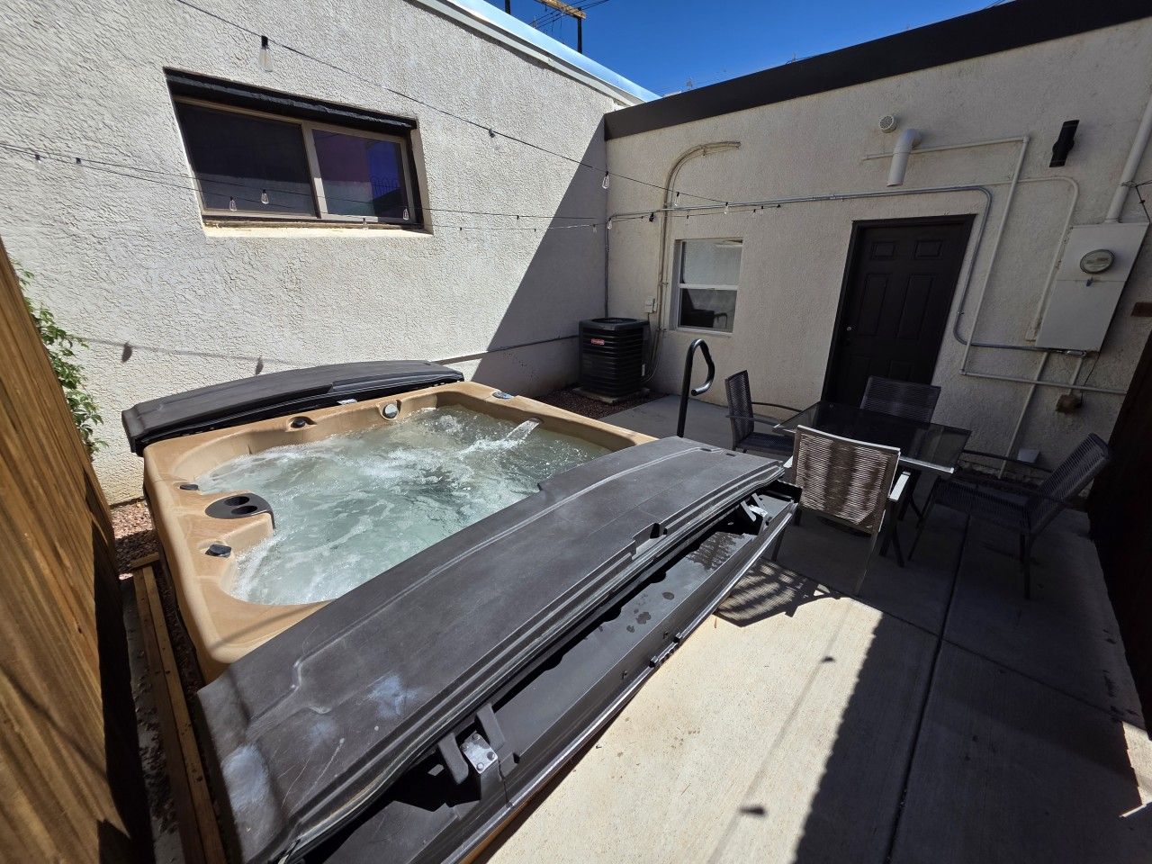 Un jacuzzi en un patio trasero con una mesa y sillas, una ventana y una puerta.