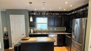 Cocina moderna con armarios oscuros, refrigerador de acero inoxidable, una isla central con encimera de madera y luminarias colgantes.