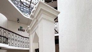 Un amplio atrio con una columna blanca central, suelo de piedra y un banco de madera.