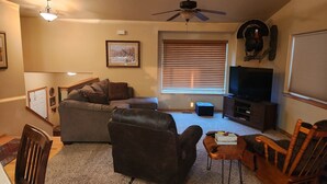A living room with a couch, a chair, a television, and a ceiling fan. - South Dakota Black Hills rental (Whitewood,)