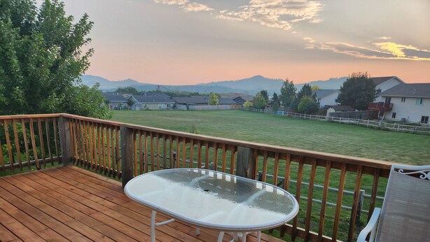 A wooden deck with a glass table and metal chairs, overlooking a grassy yard and houses in the distance. - South Dakota Black Hills rental (Whitewood,)