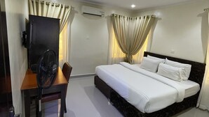 A hotel room with a bed, a desk with a chair, an air conditioner, and curtains. - NUMBER ELEVEN HOTEL (Lagos)