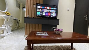 A living room with a flat-screen TV mounted on a wall, a wooden coffee table with a magazine, and a shaggy rug. - NUMBER ELEVEN HOTEL (Lagos)