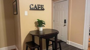 A hallway with a round table and two stools, a potted plant, and a 'CAFE' sign on the wall.