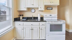 A kitchen with white cabinets, a stove, and a clock on the wall.