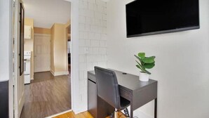 A room with a desk, chair, potted plant, and a TV mounted on the wall.