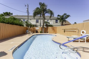 Une piscine entourée d’une clôture en bois, avec des chaises longues et un palmier.