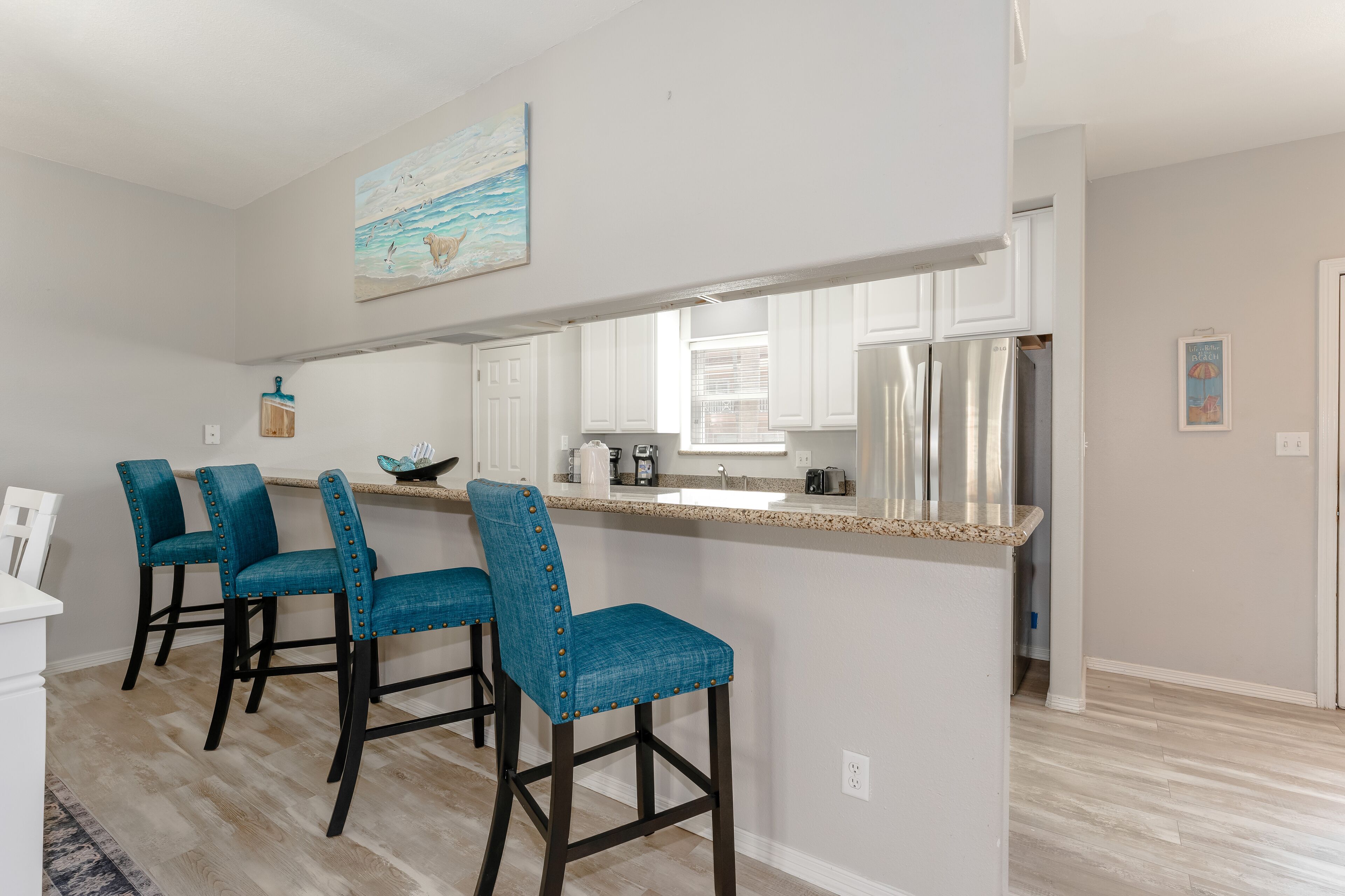 A kitchen with a central island, bar stools, and a painting above the island.
