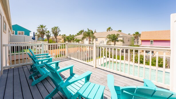 Una terraza de madera con sillas turquesa, una piscina y una barandilla blanca.