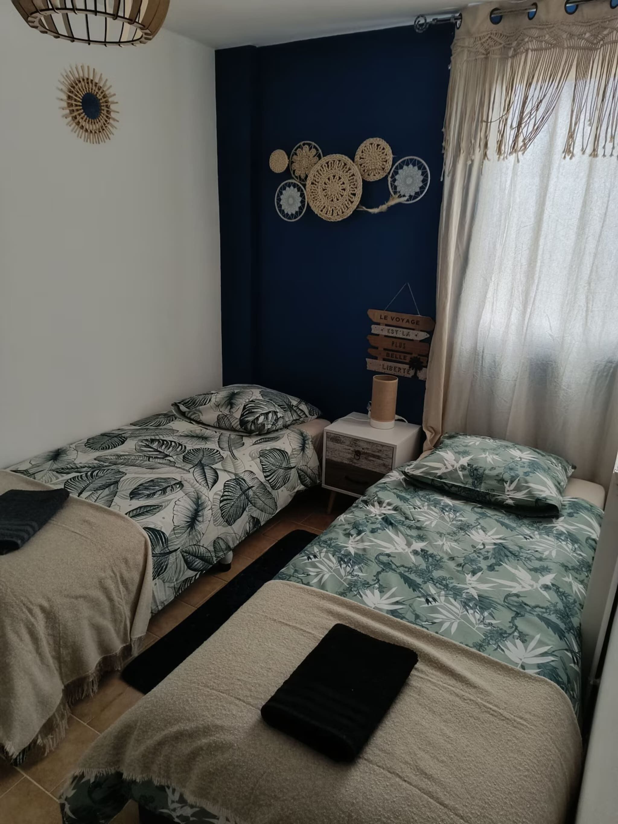 Une chambre avec deux lits, une table de chevet, une horloge murale et une fenêtre avec des rideaux.