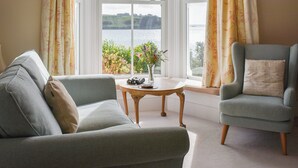 A living room with a sofa, armchair, and a small table with a vase of flowers. - 3 bedroom accommodation in St Mawes (St Mawes)