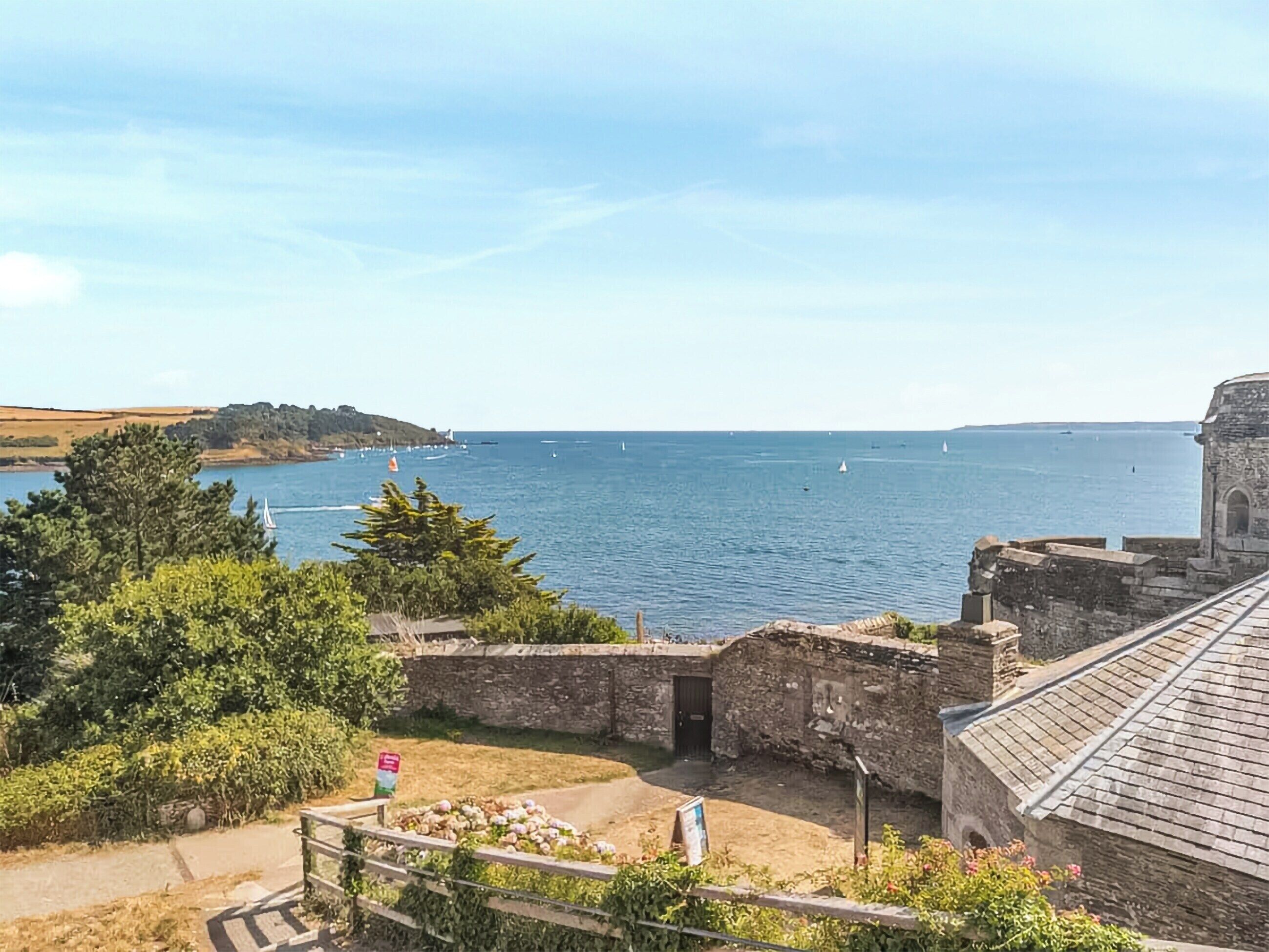 A coastal view with a stone building, a clear sky, and a distant island.