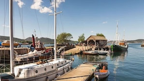 Un port de plaisance où sont amarrés plusieurs bateaux, une jetée en bois et un petit bâtiment doté d’un toit de chaume.