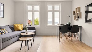 Un salon moderne avec un canapé gris, une petite table ronde et un coin repas comprenant deux chaises.
