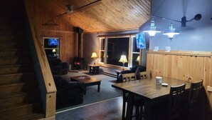 A cozy cabin interior with a fireplace, wooden walls, a TV, and a dining area. - A short walk to a private beach for swimming boating or fishing  (Arcade)