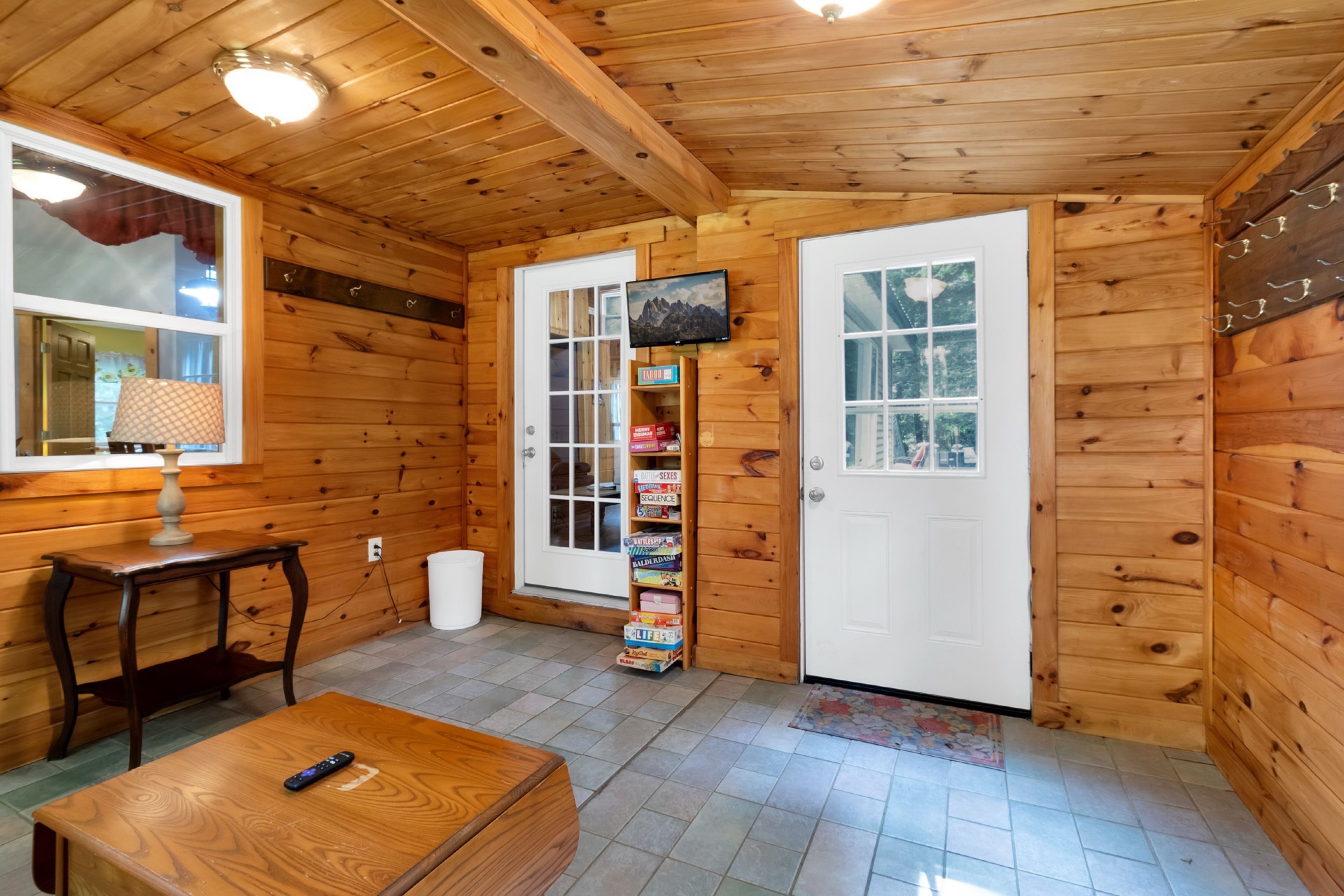 A wooden interior with a door, a small table, a lamp, and a shelf with books.