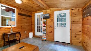 A wooden interior with a door, a small table, a lamp, and a shelf with books.